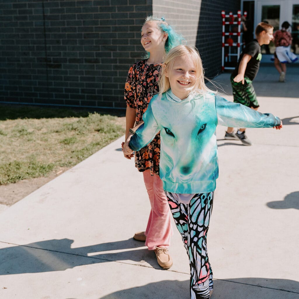 Two girls smiling and holding hands on sidewalk.