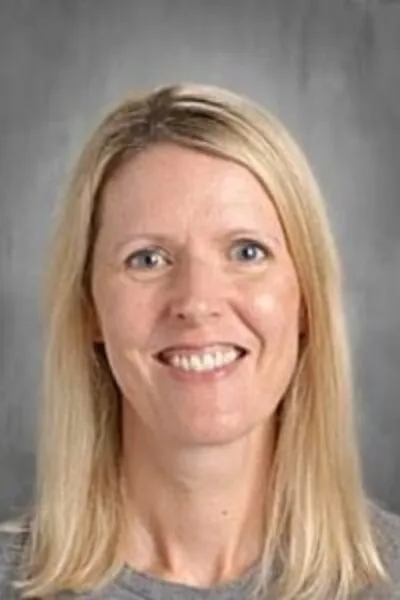 Smiling woman with straight blonde hair in front of a gray mottled studio background.